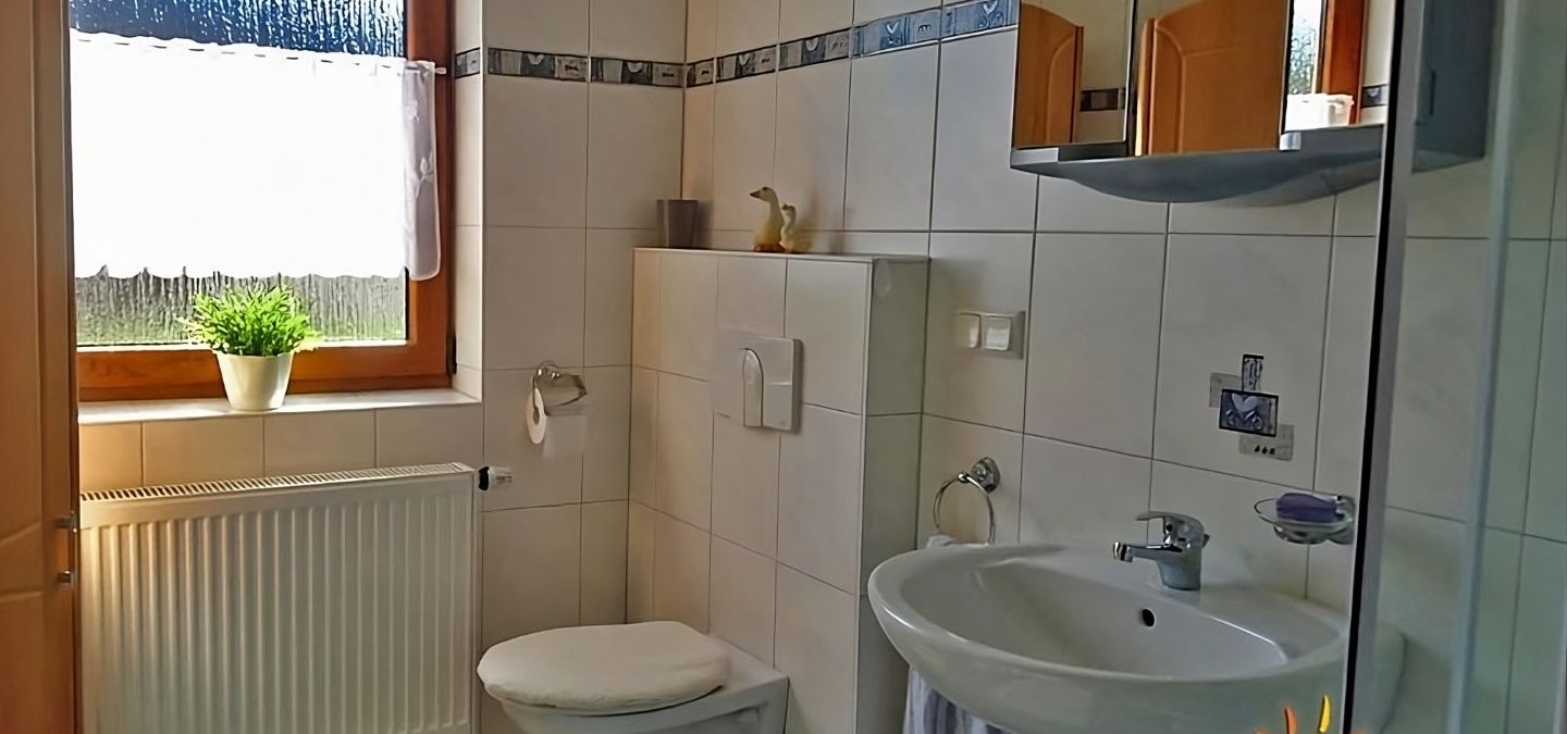 Modernes, hell gefliestes Badezimmer der Ferienwohnung Ilona in Zweibrücken mit Fenster, Waschbecken, wandhängendem WC, Spiegel und freundlicher, sauberer Atmosphäre.