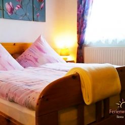 Gemütliches Schlafzimmer der Ferienwohnung Ilona in Zweibrücken mit großem Holzbett, warmem Licht, weichen Bettwaren und freundlicher Wohlfühlatmosphäre.