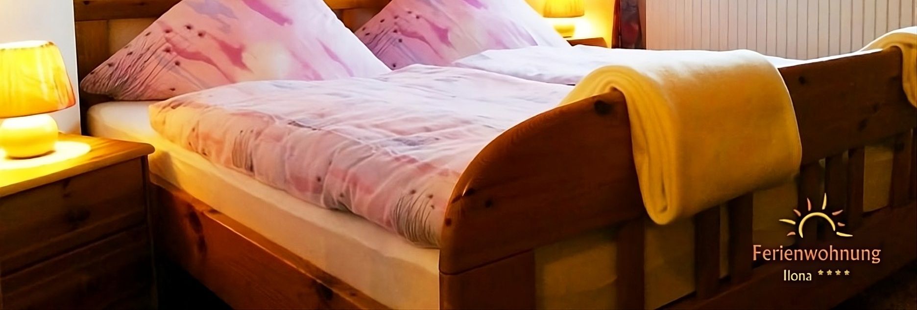 Gemütliches Schlafzimmer der Ferienwohnung Ilona in Zweibrücken mit großem Holzbett, warmem Licht, weichen Bettwaren und freundlicher Wohlfühlatmosphäre.